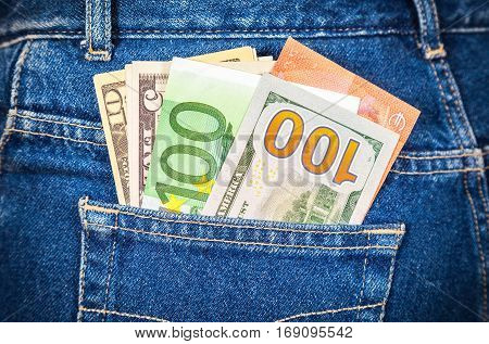 Different banknotes of Euro and american currency sticking out of the back jeans pocket. Money in jeans pocket for travel and shopping