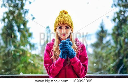 young girl in a knitted cap and mittens standing under snowing forest