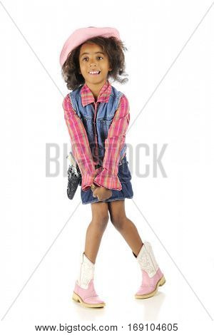 An elementary African American standing in her cowgirl outfit in an awkward position -- knees together, toes apart.  Isolated on white.
