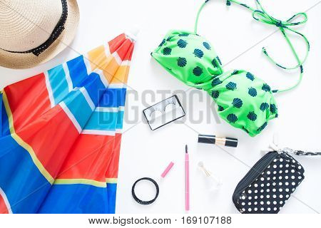 Flat lay of summer fashion with green color swimsuit colorful beach umbella and girl accessories on white background