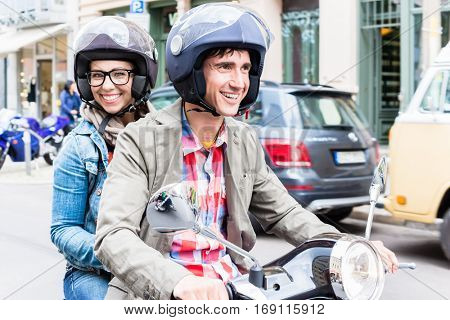 Young woman with helmet sitting on pillion seat of Vespa in streets of Berlin