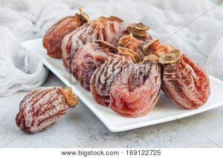 Several dried persimmon on white plate gray concrete background horizontal