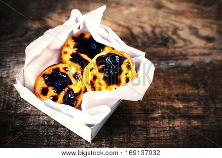 Pasteis de Nata - creamy egg tart with sweet curstard black crust and sugar powder on wooden background. Pasteis de Belem pastry