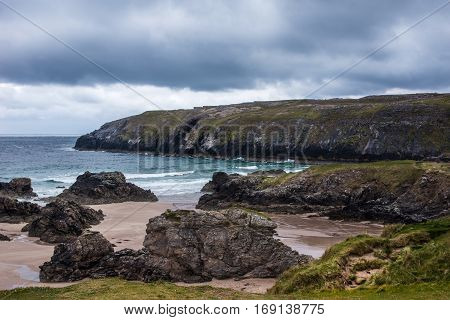 North Coast Scotland - June 6 2012: Cliffs descend on Durness Beach a sandy patch looking north on a rough coast among rock cliffs and sprinkled pieces of rock.
