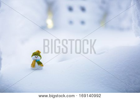 A little snowman friend stands in a cap among the white snow and behind it there is an interesting snow-covered textured window with six squares.