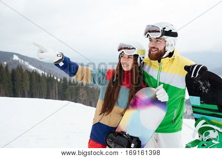 Photo of loving couple snowboarders on the slopes frosty winter day pointing. Look aside.