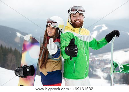 Photo of cheerful loving couple snowboarders on the slopes frosty winter day making thumbs up gesture. Look at camera.