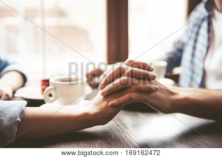 Happy young couple is drinking coffee talking and smiling while sitting at the cafe