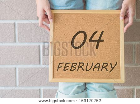 Closeup calendar at the cork board in hand of asian woman in front of her legs with 4 february word on brick wall textured background