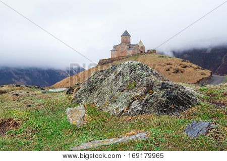 Gergeti Trinity Church Or Tsminda Sameba in the morning mist near village Stepantsminda, Georgia. Mount Kazbegi. Spring Or Summer Season.