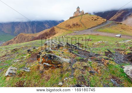 Gergeti Trinity Church Or Tsminda Sameba in the morning mist near village Stepantsminda, Georgia. Mount Kazbegi. Spring Or Summer Season.