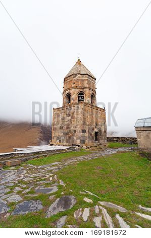 Gergeti Trinity Church Or Tsminda Sameba in the morning mist near village Stepantsminda, Georgia. Mount Kazbegi. Spring Or Summer Season.