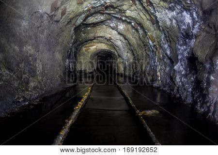 Flooded tunnel of an old abandoned coal mine with rusty remnants of railroad