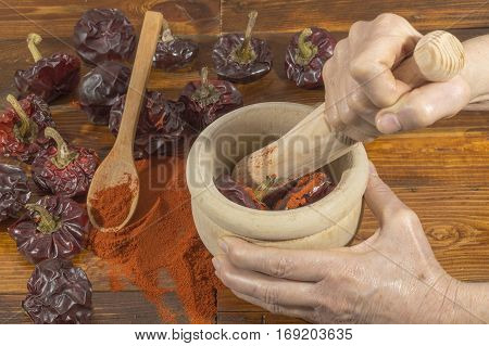 A person crushes dry red peppers with mortar