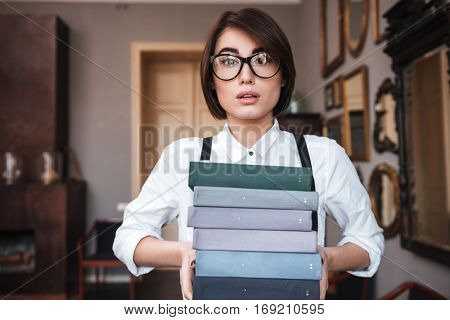 Authoress in glasses and white shirt holding books in hands and looking at camera