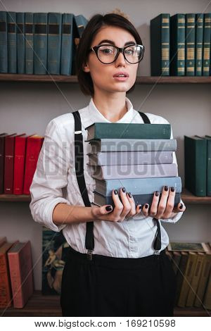 Vertical image of Authoress in glasses and white shirt holding books and looking at camera