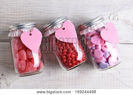 Canning jars laying on their sides filled with candy hearts and for Valentine's Day on a rustic wood table. The jars have blank heart shaped gift tags hanging from the neck.