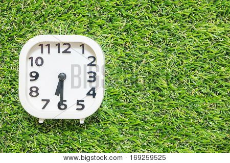 Closeup white clock for decorate show a half past six or 6:30 a.m. on green artificial grass floor textured background with copy space