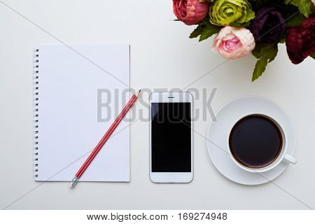 A mid shot of notebook, pencil mobile phone, cup of coffee and circle of colorful peonies on flat layout. Image of daily needs