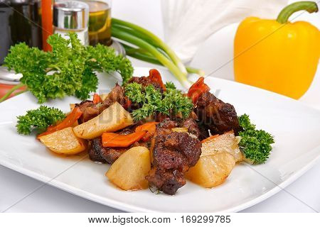 Brisket baked with potatoes on a white plate decorated with by greenery