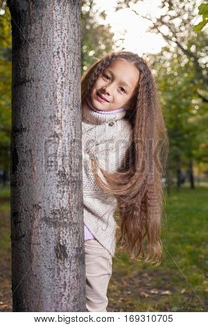 Beautiful little girl in white sweater posing in autumn Park near the tree