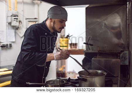 Young male chef in black uniform cooking in restaraunt kitchen