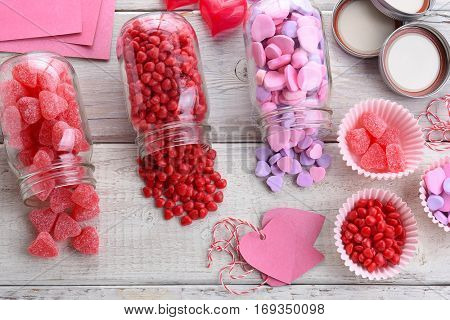 High angle view of different Valentines Day Candies on a rustic white wood table. Canning jars on their sides with candy spilling out.