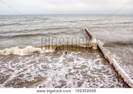 breakwater covered by ice breaking waves on cold gloomy winter day