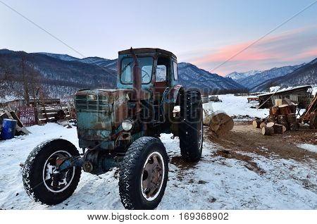 Caucasus Russia - Feb 18 2012: Old rusty soviet tractor shown on courtyard farmhouse in village in mountain region of Caucasus mountain at sunrise in winter time