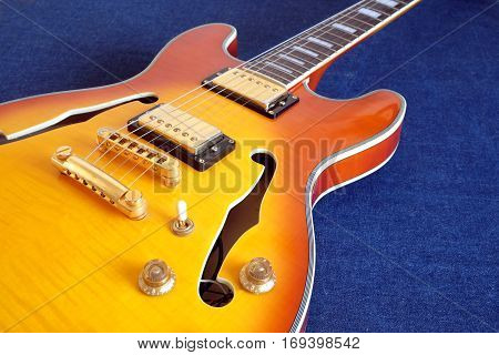 Part of vintage semi-hollow body electric guitars with pickups, electronics knobs and metal accessories on jeans background closeup