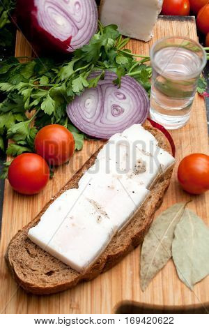 Lard on bread tomatoes onions fresh herbs and vodka on the table