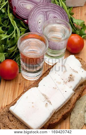 Lard on bread tomatoes onions fresh herbs and vodka on the table