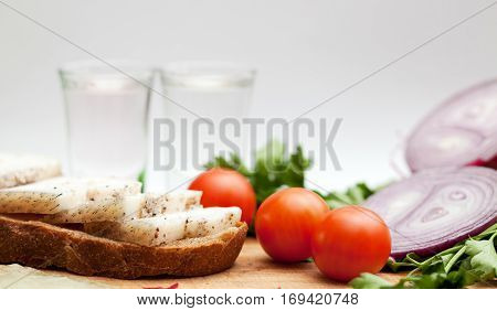 Lard on bread tomatoes onions fresh herbs and vodka on a white background