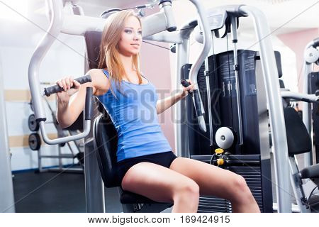 Pretty Caucasian smiling woman is working out on butterfly machine. Young Bodybuilder Doing Exercise For Chest In The Gym.