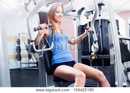 Pretty Caucasian smiling woman is working out on butterfly machine. Young Bodybuilder Doing Exercise For Chest In The Gym.