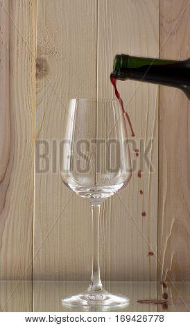 red wine being poured into a glass bottle of red wine with a brilliant glass on a wooden background on a glass stand