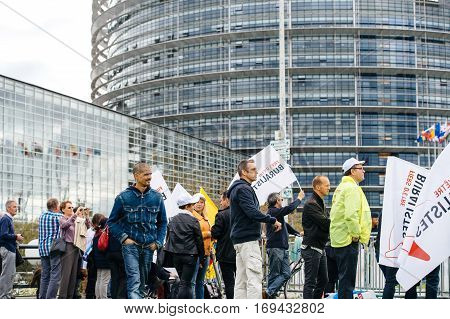 STRASBOURG FRANCE - OCT 7 2015: Rear view of tobacconists buralistes people protesting in front of the European Parliament building with flags placards while President Francois Hollande is entering the Parliament gates Confederation des buralistes