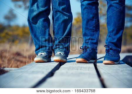 Close-up of female and kid feets in sneakers running outdoors on wooden trail, Kemeri national park, Latvia