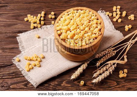 Raw pasta ditalini and rye ears in a wooden bowl on the table top view
