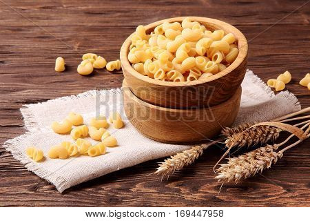 Raw elbow macaroni and rye ears in a wooden bowl on the table
