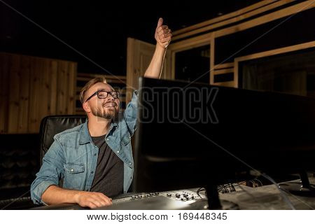 music, technology, gesture and people concept - happy man at mixing console in sound recording studio showing thumbs up