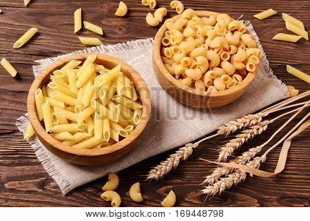 Raw pasta penne and elbow macaroni in a wooden bowls on the table
