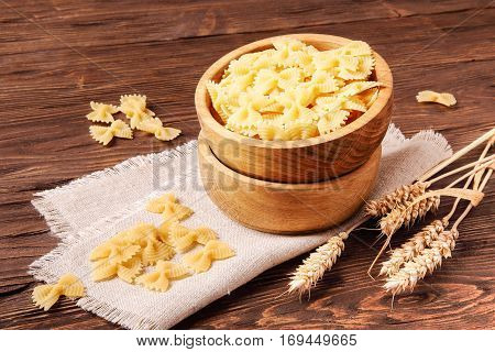 Pasta farfalle and rye ears in a wooden bowl on the table