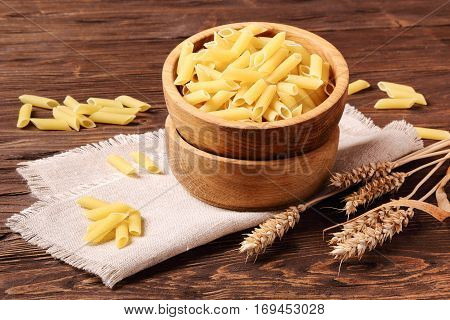 Raw pasta penne and rye ears in a wooden bowl on the table