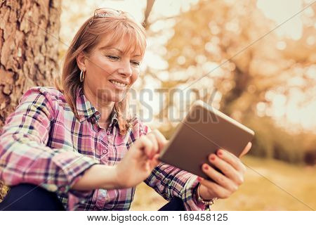 Beautiful mature woman in the park using a digital tablet.