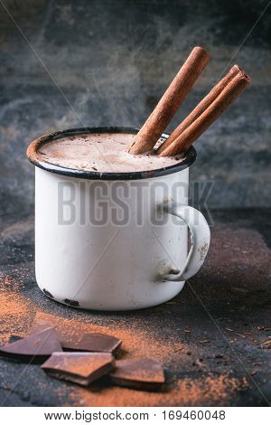 Vintage mug of hot chocolate with cinnamon sticks over dark background