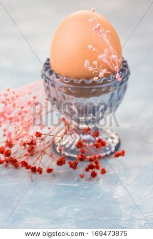 Easter egg in crystal cup spring red and pink small flowers burning candle in the background decorationtable settingelegantretro style