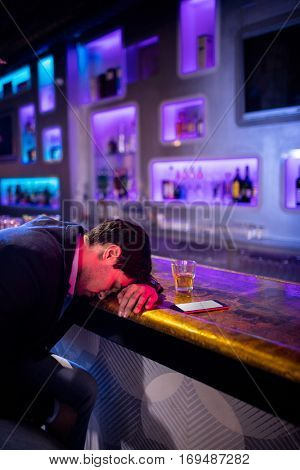 Depressed man having whisky drink at bar counter in bar