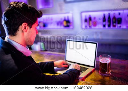 Man using laptop with glass of beer on table at bar counter in bar