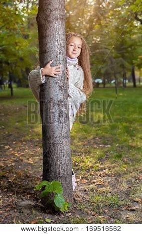Beautiful little girl in white sweater posing in autumn Park near the tree